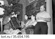 Семейный портрет супругов с дочерьми и котом в домашней обстановке, девочка подросткового возраста держит баян в руках, настенные ковры позади них, Якутия, февраль 1960. Редакционное фото, фотограф Варфоломей Тетерин / Фотобанк Лори