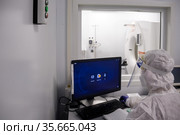 Врач в защитном костюме от коронавируса сидит перед монитором компьютерного томографа в кабинете медицинского центра ​помощи и спасения. Богучаны, Красноярский край, Россия (2021 год). Редакционное фото, фотограф Светлана Попова / Фотобанк Лори