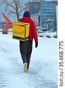 Пеший курьер службы Glovo с желтой термосумкой на улице Киева, Украина (2021 год). Редакционное фото, фотограф FMRU / Фотобанк Лори