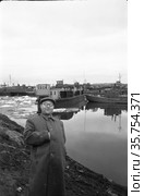 Человек средних лет позирует стоя на берегу реки Лена, он засунул правую руку под плащ, мужчина на фоне проходов, Якутия, 22 май 1958. Редакционное фото, фотограф Варфоломей Тетерин / Фотобанк Лори