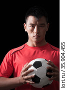 Footballer holding ball to chest, black background. Стоковое фото, агентство Ingram Publishing / Фотобанк Лори