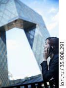 Smiling businesswoman on the phone outside in Beijing looking at the CCTV building. Стоковое фото, агентство Ingram Publishing / Фотобанк Лори