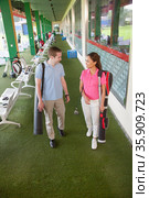 Young happy couple leaving the golf course with golf clubs and caddy. Стоковое фото, агентство Ingram Publishing / Фотобанк Лори