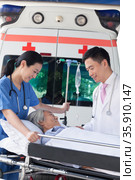 Female paramedic and doctor wheeling in a elderly patient on a stretcher in front of an ambulance. Стоковое фото, агентство Ingram Publishing / Фотобанк Лори