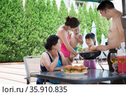Smiling multi-generational family barbequing by the pool on vacation. Стоковое фото, агентство Ingram Publishing / Фотобанк Лори