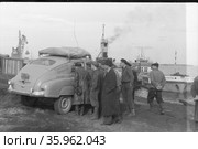 Молодые люди заглядывают в автомобиль марки Победа, они находятся на берегу водоёма, стрела погрузочного крана и речной паром на заднем плане, поездка Владивосток-Кронштадт, 1958. Редакционное фото, фотограф Варфоломей Тетерин / Фотобанк Лори