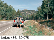 a man and a woman autotourists stand on the highway near the car and point to the high mountain Aleksandrovskaya Sopka on a sunny summer day. Стоковое фото, фотограф Акиньшин Владимир / Фотобанк Лори