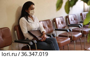 Focused adult hispanic woman in protective face mask sitting on chair in office corridor, waiting for job interview. Pandemic precautionary concept. Стоковое видео, видеограф Яков Филимонов / Фотобанк Лори