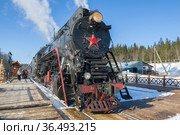 Старый советский паровоз ЛВ-0522 с туристическим ретро поездом "Рускеальский экспресс" прибыл на станцию Рускеала солнечным мартовским днем. Карелия (2021 год). Редакционное фото, фотограф Виктор Карасев / Фотобанк Лори
