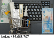 Концепция покупки лекарств в интернете. Игрушечная тележка для продуктов с таблетками, бинтом, медицинским градусником, российские деньги на клавиатуре ноутбука. Стоковое фото, фотограф Цибаев Алексей / Фотобанк Лори