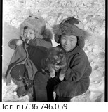 Два ребенка сидят на снегу и показывают маленького щенка, фотопортрет детей сидящих в теплой зимней одежде, кутенок в руках детей дошкольного возраста, мальчик и девочка. Редакционное фото, фотограф Варфоломей Тетерин / Фотобанк Лори