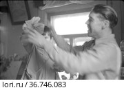 Мужчина одевает бант на маленькую девочку, отец наряжает малышку, стоя рядом с большим окном, семейный портрет с ребенком в домашней обстановке. Редакционное фото, фотограф Варфоломей Тетерин / Фотобанк Лори