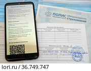 Российский полис обязательного медицинского страхования и сертификат о проведении по вакцинации против COVID-19, смартофон с открытым сайтом государственных услуг и QR кодом (2021 год). Редакционное фото, фотограф Цибаев Алексей / Фотобанк Лори