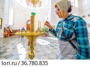 an elderly woman to put a candle in a candlestick in a church for a commemoration (2021 год). Редакционное фото, фотограф Акиньшин Владимир / Фотобанк Лори