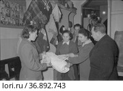 Женщины выбирают ткань на ярмарке, продавец демонстрирует девушки занавеску свернутую в рулон, покупатели в магазине, Якутия, январь 1969, ярмарка в Холбосе. Редакционное фото, фотограф Варфоломей Тетерин / Фотобанк Лори