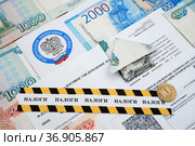 Извещение из налоговой инспекции, дом, сложенный из купюры и оградительная лента с надписью "налоги" (2021 год). Редакционное фото, фотограф Цибаев Алексей / Фотобанк Лори