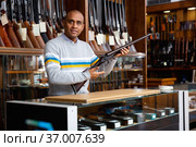 Hispanic salesman showing collectible rifled musket in gun store. Стоковое фото, фотограф Яков Филимонов / Фотобанк Лори
