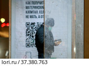 Мужчина на остановке смотрит в смартфон на фоне плаката с информацией о материнском капитале для отцов (2022 год). Редакционное фото, фотограф Сайганов Александр / Фотобанк Лори