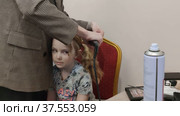 Стилист делает модную красивую прическу ребенку. The stylist makes a fashionable beautiful hairstyle for the child. Редакционное видео, видеограф Мария / Фотобанк Лори