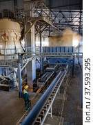 Aktobe region, Kazakhstan - May 04 2019: Phosphate fertilizers plant. Machine for pellets production. Operator in yellow helmet controls process. Редакционное фото, фотограф Alexey Rezvykh / Фотобанк Лори