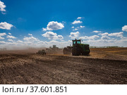 North Kazakhstan Province, Kazakhstan - May 12, 2012: Sowing campaign. John Deere tractors cultivating soil with harrow. Blue sky, clouds. Редакционное фото, фотограф Alexey Rezvykh / Фотобанк Лори