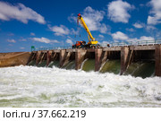 Kok-aral, Kazakhstan - May 03, 2012: Small Aral Sea Kok-aral dam. Water discharge in flood. Open shutters. Yellow mobile crane and workers on dam. Стоковое фото, фотограф Alexey Rezvykh / Фотобанк Лори