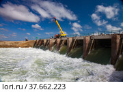 Kok-aral, Kazakhstan - May 03, 2012: Small Aral Sea Kok-aral dam. Water discharge in flood. Open shutters. Yellow mobile crane and workers on dam. Стоковое фото, фотограф Alexey Rezvykh / Фотобанк Лори