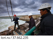 Kok-aral, Kazakhstan - May 03, 2012: Small Aral Sea Kok-aral dam. Hydraulic engineers prepair to lift water shutter weights. Crane's steel rope with hooks. Stormy sky and turbulent water. Редакционное фото, фотограф Alexey Rezvykh / Фотобанк Лори