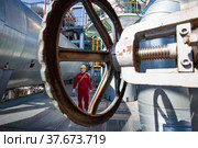 Aktobe region/Kazakhstan - May 04 2012: Oil refinery plant. Asian refinery worker and steering wheel or valve. On refinery column and tank background. CNPC company. Редакционное фото, фотограф Alexey Rezvykh / Фотобанк Лори