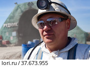 Khromtau, Aktobe region, Kazakhstan - May 06 2012: Gold ore mining. Portrait of miner in white protective suit, protective glasses, white work helmet and headlight. Blurred mine portal on background. Редакционное фото, фотограф Alexey Rezvykh / Фотобанк Лори