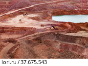 Aluminium ore quarry and blue quarry lake in bauxite mine. Yellow excavators and dump trucks. White road. Open cast (open-cut) mining. Стоковое фото, фотограф Alexey Rezvykh / Фотобанк Лори