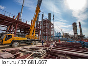 Aktau, Kazakhstan - May 19, 2012: Construction of asphaltic bitumen plant refinery column. Metal distillation tower and yellow hydraulic hoist. Редакционное фото, фотограф Alexey Rezvykh / Фотобанк Лори