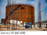 Aktau, Kazakhstan - May 19, 2012 Construction of modern asphaltic bitumen plant. Group of workers, concrete mixer truck and Rusty oil storage tank. On blue sky background. Стоковое фото, фотограф Alexey Rezvykh / Фотобанк Лори