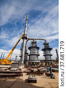 Aktau, Kazakhstan - May 19, 2012: Construction of asphaltic bitumen plant refinery column. Distillation tower and yellow hydraulic hoist. Редакционное фото, фотограф Alexey Rezvykh / Фотобанк Лори