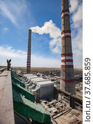 Grey raw coal bunkers on front. Smoke stacks with white smoke both sides. Dry steppe, blue sky on background. Ekibastuz, Pavlodar reg., Kazakhstan. GRES-1 thermal power station. Стоковое фото, фотограф Alexey Rezvykh / Фотобанк Лори