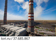 GRES-1 thermal power station. Raw coal bunkers on front. Two smoke stacks. Coal-harvesters in dust loading coal to electricity plant. Dry steppe and blue sky. Ekibastuz, Pavlodar reg., Kazakhstan. Стоковое фото, фотограф Alexey Rezvykh / Фотобанк Лори