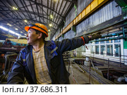 Aksu, Pavlodar region, Kazakhstan - May 29, 2012: Aksu steam power station. Asian worker in orange hardhat show hand signals to crane operator. Blurred industrial interior background. Редакционное фото, фотограф Alexey Rezvykh / Фотобанк Лори