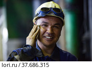 Aksu, Pavlodar region, Kazakhstan - May 29, 2012: Aksu steam power station. Portrait of young smiling asian worker in yellow hardhat. Cleaning mud with tissue. Blurred background. Редакционное фото, фотограф Alexey Rezvykh / Фотобанк Лори