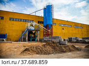 Temirtau, Kazakhstan - June 09, 2012: Concrete sleepers manufacturing plant NORD Prom NS. Blue cement and sand mixing silos. Industrial building with yellow thermal insulation. Редакционное фото, фотограф Alexey Rezvykh / Фотобанк Лори