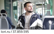 Young bearded man traveler riding in modern streetcar, standing leaning on suitcase and holding on to handrails. Стоковое видео, видеограф Яков Филимонов / Фотобанк Лори