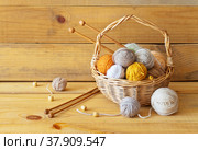 Clews of warm soft wool and mohair yarn lie in a wicker basket with wooden knitting needles. Rustic still life on a wooden background. The concept of needlework, hobbies and knitting. Closeup, copy space. Стоковое фото, фотограф Виктория Катьянова / Фотобанк Лори