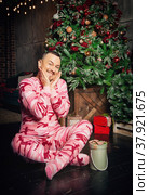 Cheerful surprised funny man in pink sleepwear sitting near decorated fir tree and Christmas present. Стоковое фото, фотограф Darkbird77 / Фотобанк Лори