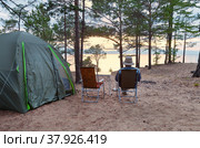 Baikal Lake on a summer evening. A tourist admires the sunset over the Small Sea Strait. Tent on the bank of Olkhon Island. Summer travel and outdoor recreation. Стоковое фото, фотограф Виктория Катьянова / Фотобанк Лори