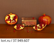 Beautiful composition with ripe pomegranates and rhodonite stone box on wooden table. Can be used as a podium for the presentation of cosmetics with fruit extracts. Front view, brown background, mock up. Стоковое фото, фотограф Виктория Катьянова / Фотобанк Лори