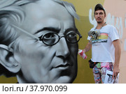 Улыбчивы уличный художник Сергей Юраков расписывает стену центральной библиотеки имени Ф.И. Тютчева в Балашихе (2022 год). Редакционное фото, фотограф Дмитрий Неумоин / Фотобанк Лори
