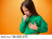 Teen girl wearing casual clothes feeling unwell and coughing against orange background. Стоковое фото, фотограф Сергей Толмачёв / Фотобанк Лори