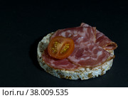 Grain crispbreads crispy rice diet bread and smoked sausage sandwich with half cherry tomato. Rice cake puffed rice with salami, sausage, balyk, smoked meat on black background. Стоковое фото, фотограф Tae Mi / Фотобанк Лори