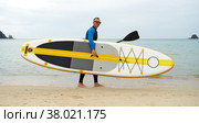 A man in a wetsuit with a yellow SUPboard and a paddle is going for a walk on the sea. Active recreation. Стоковое фото, фотограф Енваев Андрей / Фотобанк Лори