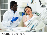 Woman patient who came to an appointment with a male dentist is sitting in a dental chair in clinic office, showing which side of her tooth aches. Стоковое фото, фотограф Яков Филимонов / Фотобанк Лори