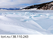 Winter landscape of snow-covered frozen Baikal Lake at frosty day in January. Ice hummocks are swept up by dense snow crust. The mountains are covered with low clouds. Cold natural background. Стоковое фото, фотограф Виктория Катьянова / Фотобанк Лори